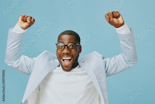 joyful celebration, African American man, blue background, business attire, glasses, excitement, professional clothing, happiness, success expression, smiling individual, modern fashion style, positi photo