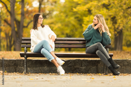 Two beautilful young women sitting on the bench in publiic park photo