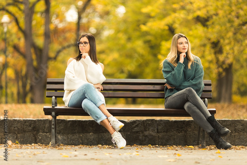 Two beautilful young women sitting on the bench in publiic park photo