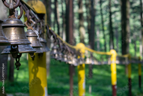 A row of brass bells on yellow pillars in a serene forest of tarkeshwar mahadev temple india.The focused details and blurred background evoke a sense of peace and spirituality, perfect for meditation. photo