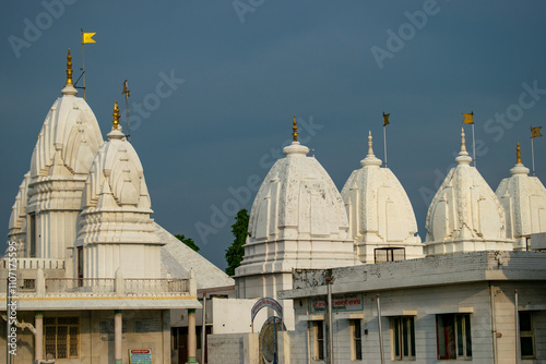 A magnificent white temple with intricate domes and golden spires, adorned with yellow flags, standing against a clear blue sky.The serene structure of jain temples in Hastinapur, uttar pradesh india.