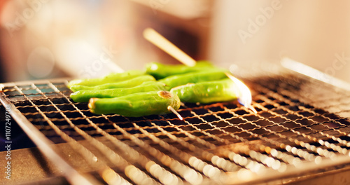 Japanese, food and green vegetable skewer on grill, outdoor barbecue or traditional kebab dinner on fire. Asian cuisine, culture and cooking pepper kushiyaki cooking on flames at local street market. photo