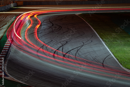 Long exposure night photography that shows the traces of light left by the racing cars as they pass through the curve. There is a line that shows an overtaking