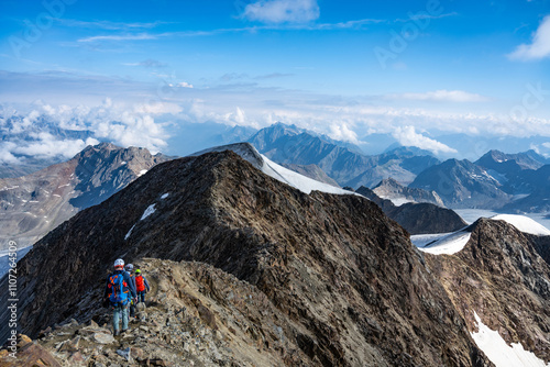 Climbers navigate the rocky terrain at the north summit of Wildspitze in Austria, surrounded by stunning mountain vistas and a clear blue sky on a perfect day for hiking.
