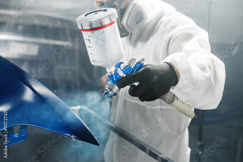 Male automobile repairman painter in protective workwear and respirator painting part of car body in paint chamber photo