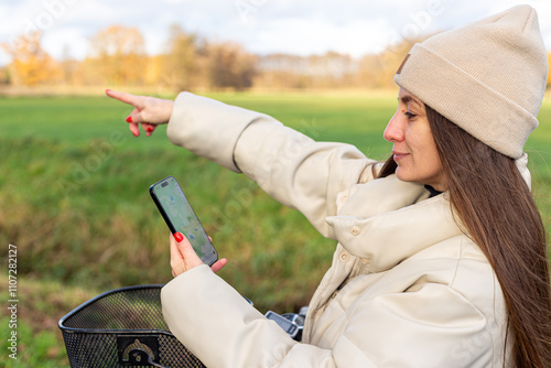 Woman using smartphone with a map app for navigation and route planning while cycling outdoors in autumn.