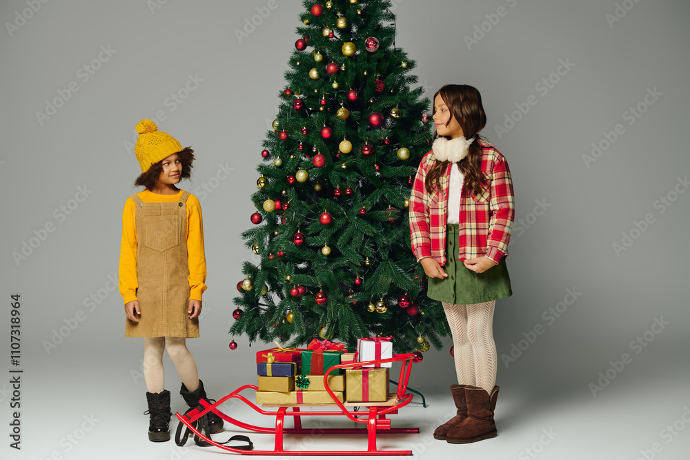 Two cheerful girls share laughter beside a festive Christmas tree with gifts nearby. Two cheerful girls share laughter beside a festive Christmas tree with gifts nearby.