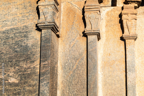 Ancient stone pillars with intricate carvings in sunlight at a historical site in a serene landscape