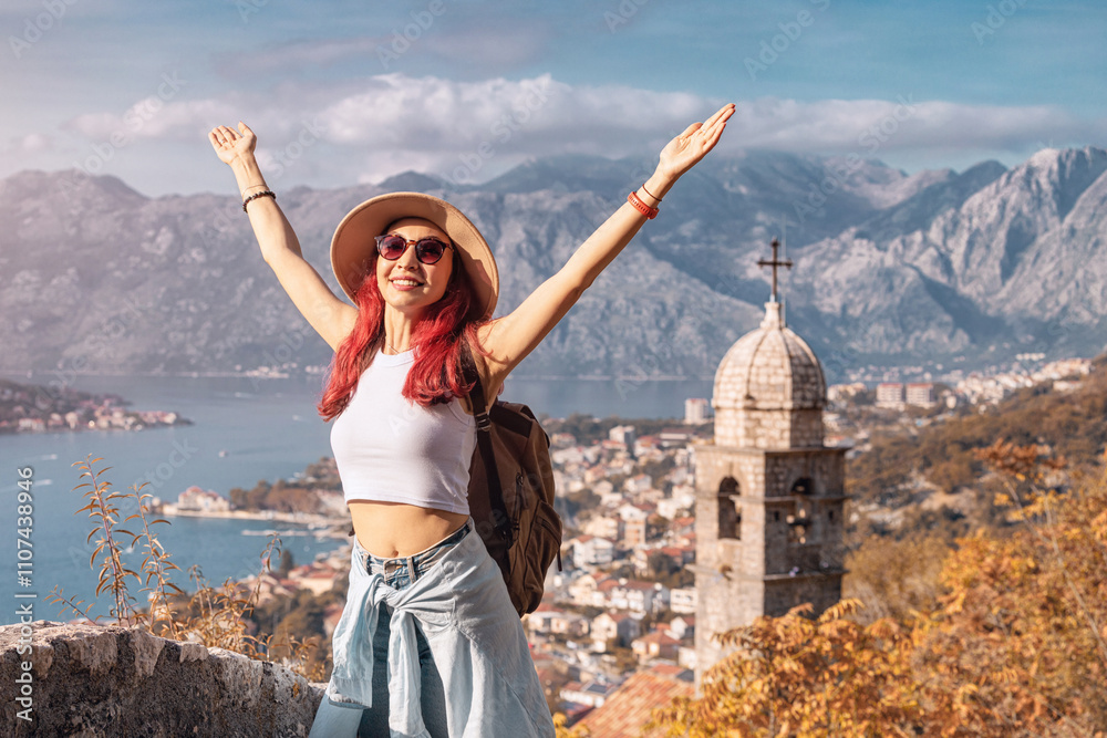 Happy tourist with backpack raising arms enjoying the view of bay of Kotor in Montenegro