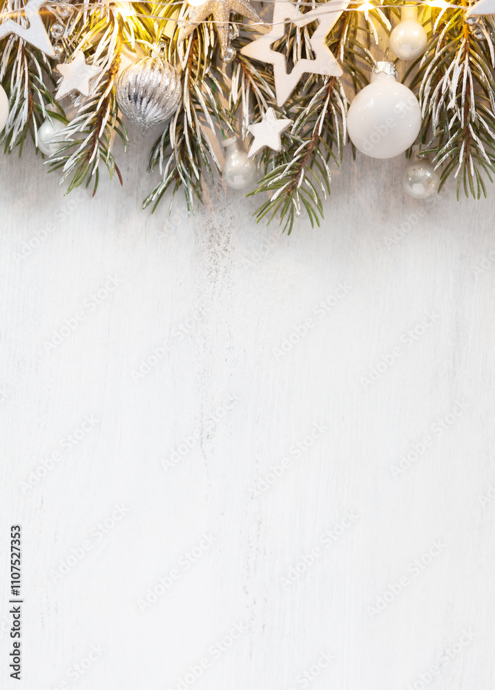 Fir branch with white Christmas ornaments and glowing garland on old wooden shabby background with empty space for text.
