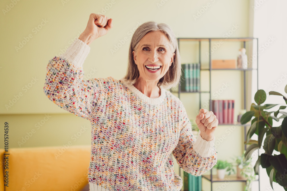 Joyful elderly woman celebrating happiness at home in colorful knitted sweater Joyful elderly woman celebrating happiness at home in colorful knitted sweater