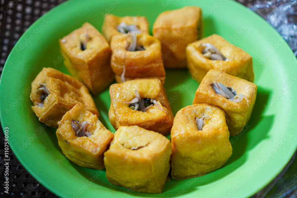 Fototapeta premium Close-up of golden-fried tofu cubes filled with bean sprouts, arranged on a green plate. A simple yet delicious Indonesian snack.