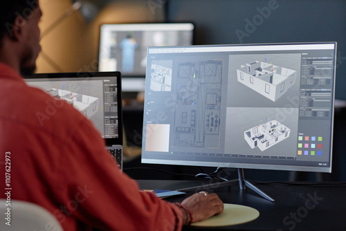 Man working on architectural designs on dual computer screens in an office environment. Concentrating on details of building layout and structure on screen