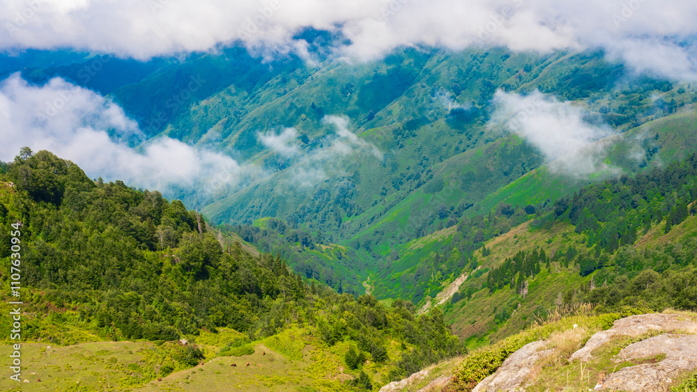 Fototapeta premium Bright clouds hover above a lush mountain landscape under clear blue skies