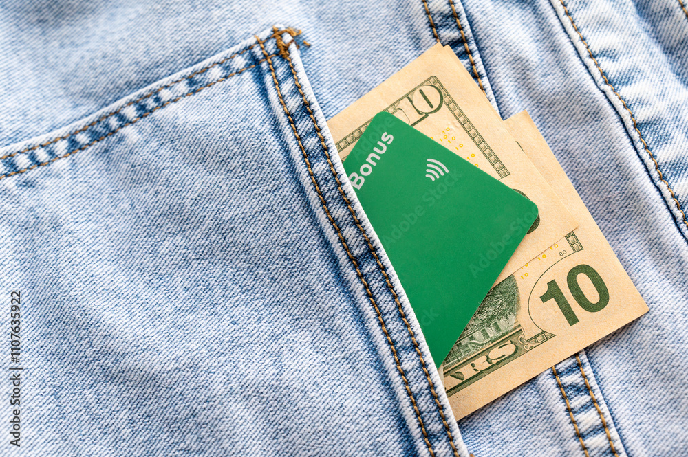 Contactless payment credit card and US dollar bills in the pocket of blue denim jeans, representing modern payment methods alongside traditional cash