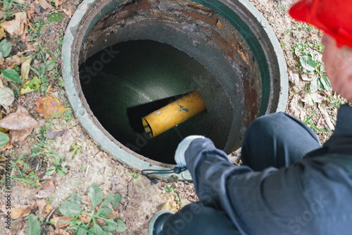 A worker with a flashlight inspects an open sewer manhole. Septic tank maintenance, sewage pumping