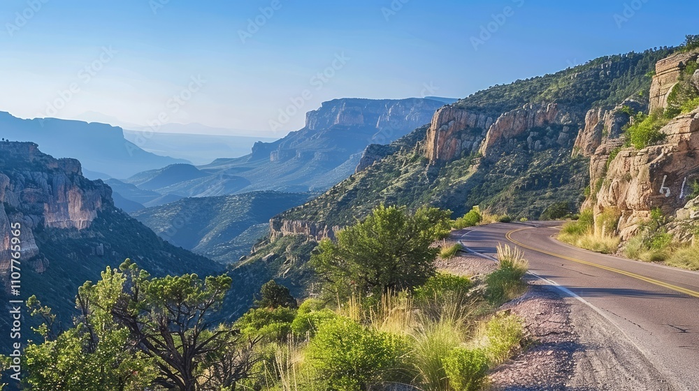 Fototapeta premium Scenic mountain road winding through lush green valleys under a clear blue sky.
