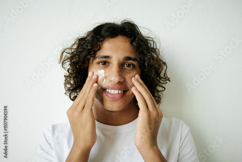 Portrait of young adult man applying cream on cheeks after shaving photo