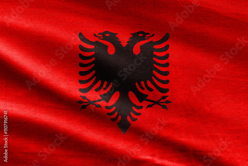 Albania flag with black double-headed eagle on a textured red fabric background.