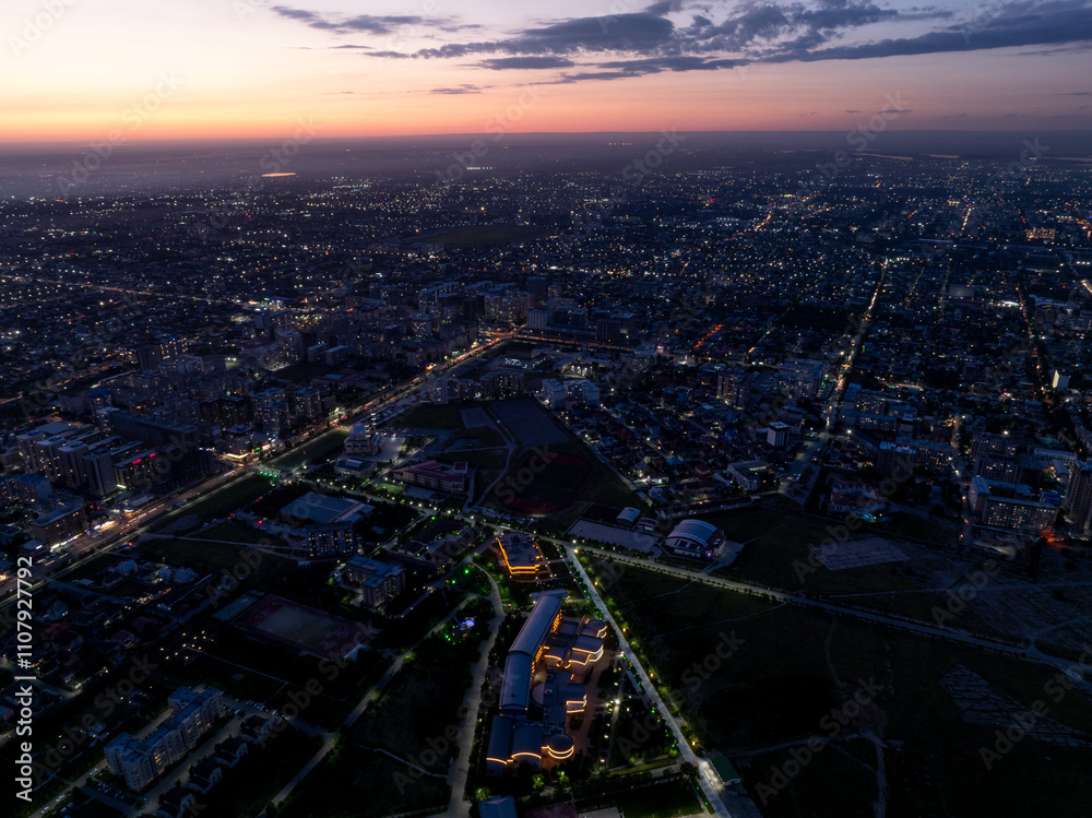 Obraz premium City landscape. Evening view from a drone of the city at sunset. Trees, roads, streets, cars and buildings. Beautiful summer scenery.