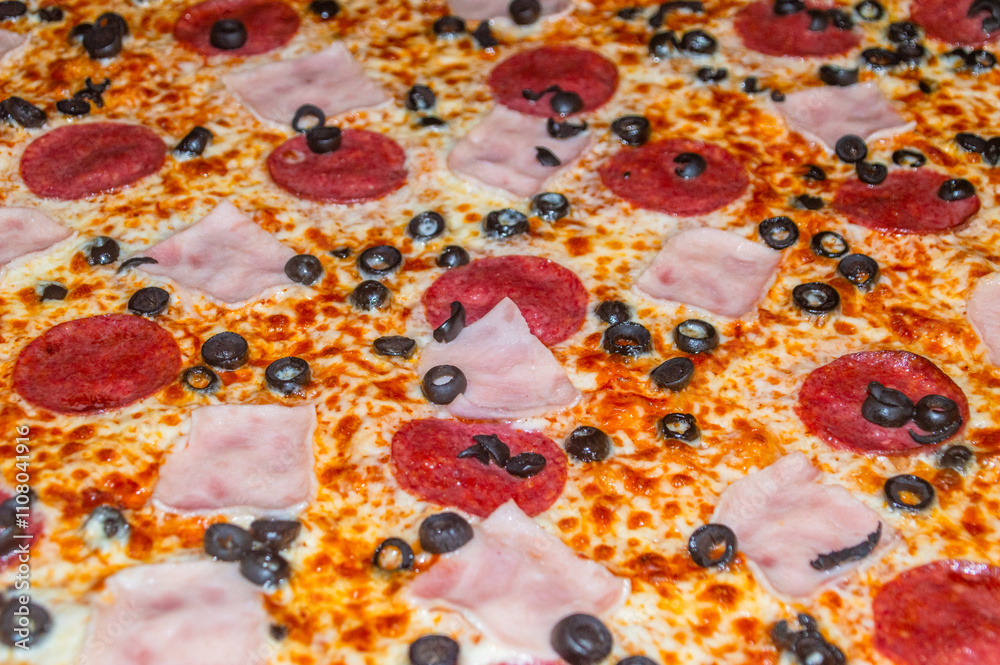 Close-up of pizza with ham, salami and black olives.