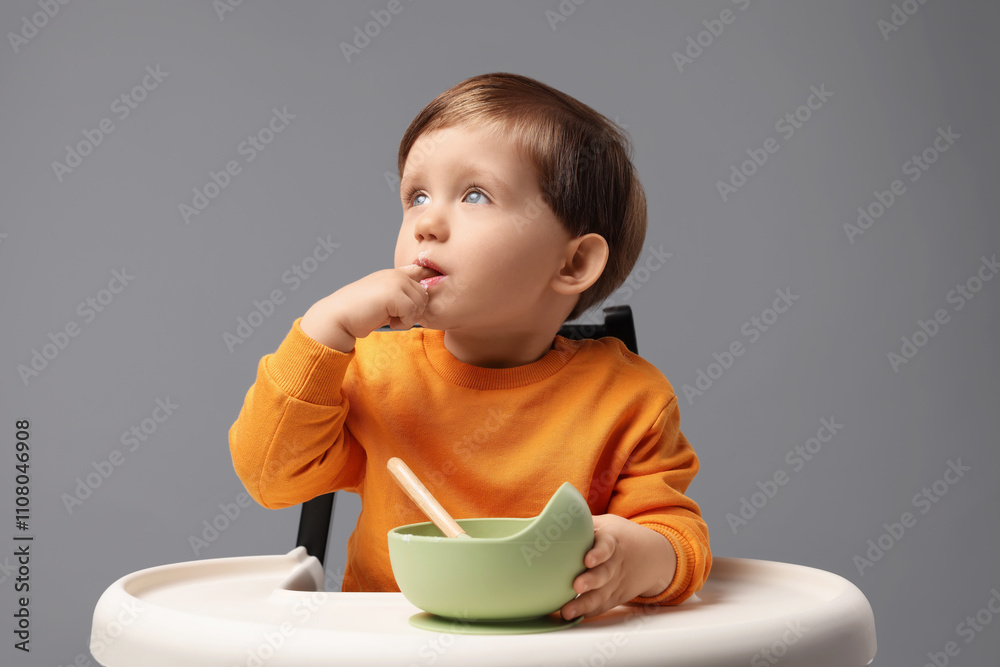 Cute little kid eating healthy baby food from bowl in high chair on light grey background Cute little kid eating healthy baby food from bowl in high chair on light grey background