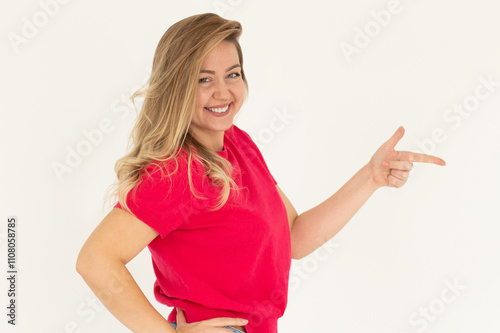 Hey look. Smiling pretty female model pointing finger right at empty space and inviting to check it out, showing advertisement on white background.