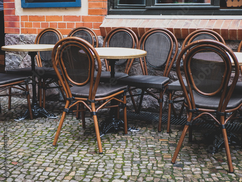 Round tables and chairs with bent backs and legs await visitors on the cafe's summer terrace