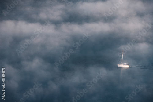Obraz na płótnie White sailboat sailing on calm sea with low clouds creating a mystical atmosphere w salonie