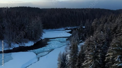 A dramatic aerial view of a wild winter forest, with a frozen river bending through the snowy terrain.
