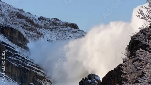 A breathtaking view of a massive snow avalanche cascading down a steep mountain range.