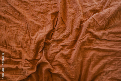 A crumpled rust-coloured fabric with organic folds. Bed linen sheets with warm, natural earthy tones.