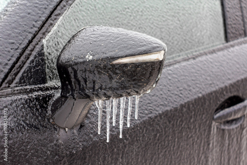 The car was iced over in winter after an icy rain. car mirror with icicles, covered with ice. Frost, rain and a car. Blurred background