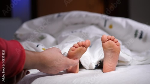 Parent tickling child's feet under blanket in bed in the mortning