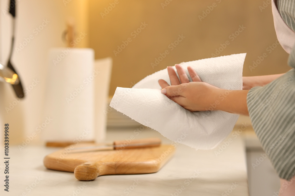 Obraz premium Woman wiping hands with paper towel in kitchen, closeup