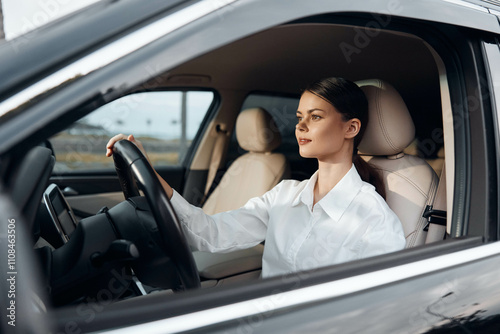 Young woman driving a car, her hand on the steering wheel, looking directly at the camera, portraying confidence and focus photo