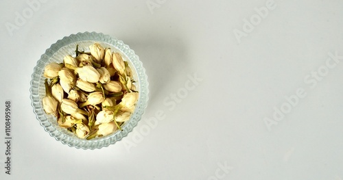 Dried jasmine flower buds for aromatheraphy and tea ingredients in round glass bowl isolated on horizontal copy spaced plain background from above angle view. photo