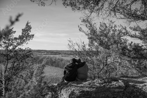 A couple sits on a rock at an overlook; watching the sunset together.