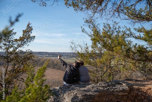 A couple sits on a rock at an overlook; watching the sunset together.