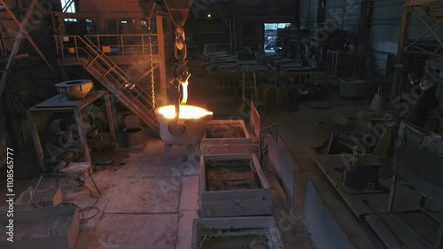 A huge ladle pours smoking metal into rectangular moulds. One of the phases of work in a steel foundry.