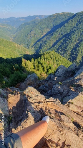 Standing on mountain top, looking down in the valley. Green pine tree forest mountains. Beautiful summer day. Rocky cliff at the end of the hiking trail. Tacla Gavrii, Marisel, Cluj, Romania photo