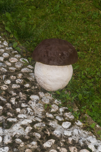 La scultura di un fungo delimita una piccola strada ad acciottolato e un prato verde in un piccolo paese di montagna in Val di Zoldo nelle Dolomiti bellunesi  photo