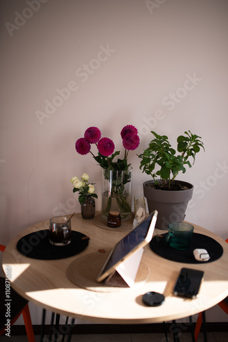 Served kitchen wooden table with pink dahlias in a glass vase. iPad, candles, cup of coffee.