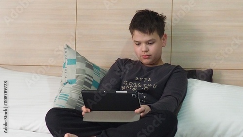 Smiling teenage school kid using tablet computer, relaxing on sofa at home, watching learning video, movie, online class, listening to music, communicates with friends, social networks