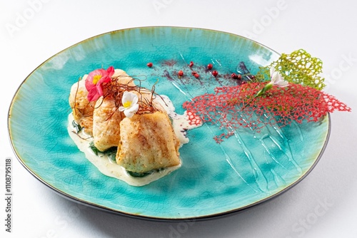 Chicken Rolls with White Sauce and Edible Flower on a Plate Against a White Background