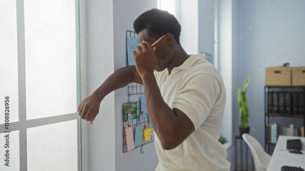 Fototapeta premium Young man leaning on a windowsill in a modern office room while holding a pen and looking contemplative