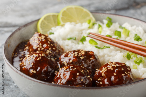 Asian meatballs coated in the sweet and spicy sauce made with sriracha, soy sauce, ginger, honey and garlic served with rice closeup on the bowl on the table. Horizontal