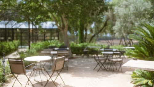 Blurred outdoor cafe setting in mallorca with defocused tables, chairs, and lush greenery in the background under bright sunlight.