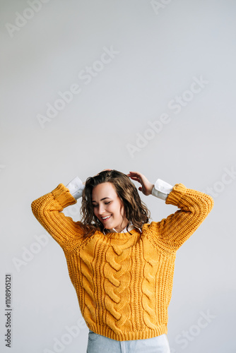 A woman in a yellow sweater is smiling and posing for the camera. The sweater is knitted and has a cable knit design. The woman's hair is styled in a ponytail