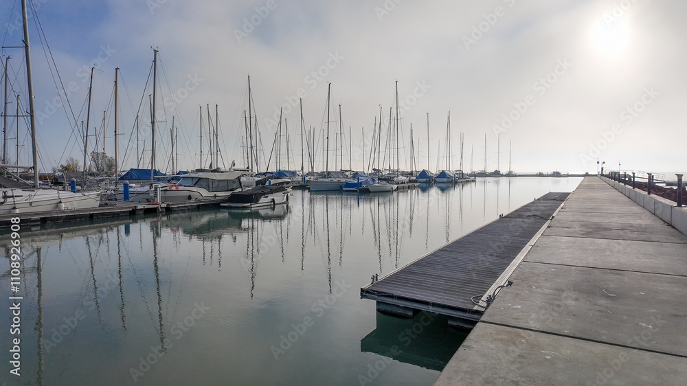 Fototapeta premium Serene marina with docked yachts under a misty sky, perfect for concepts of tranquility and coastal travel